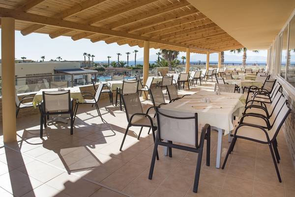Terrasse des Eurovillage Achilleas Hotels mit Tischen und Stühlen und Blick auf das Meer.