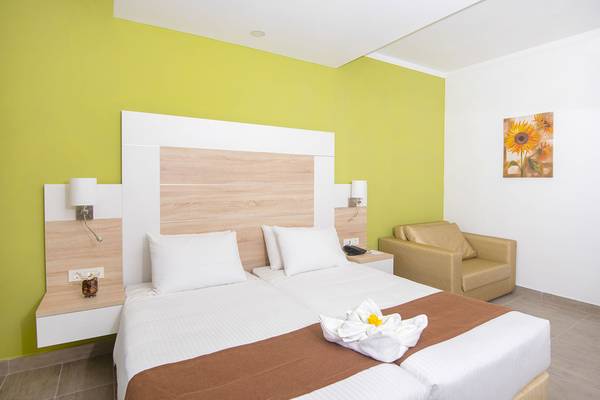 Doppelbett-Zimmer im Eurovillage Achilleas Hotel mit grüner Wand und beigem Stuhl.