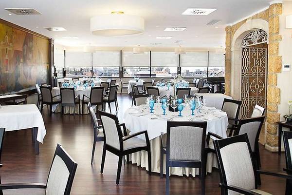 Innenansicht des Restaurants im Mundial Hotel mit runden Tischen und Stühlen, Wandgemälde und Ausblick auf die Stadt.