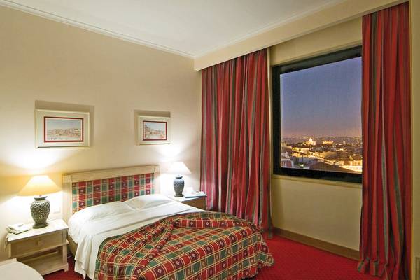 Schlafzimmer im Mundial Hotel mit Bett, Lampen und Stadtblick durch großes Fenster.