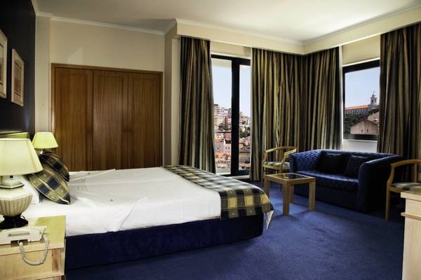 Schlafzimmer im Mundial Hotel mit Doppelbett, Sofa und Fenstern mit Stadtblick