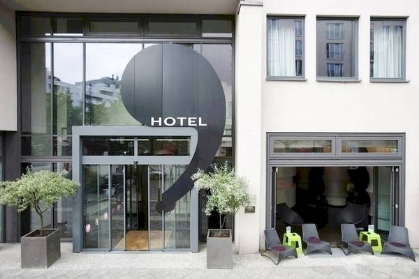 Eingang des Ku Damm 101 Hotels mit Glasfassade und schwarzen Elementen.