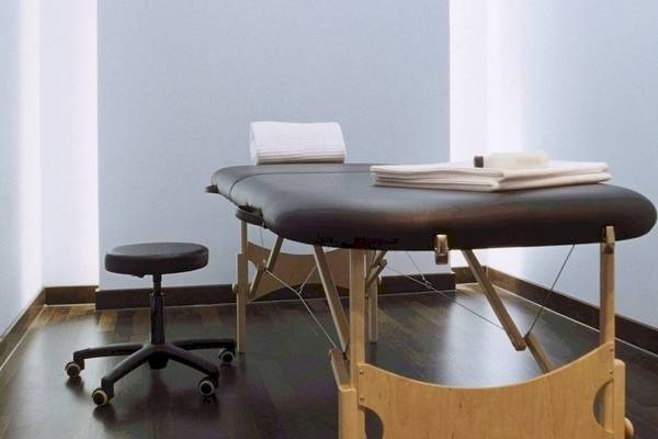 Massage-Behandlungsraum im Hotel Ku Damm 101 mit schwarzem Tisch und weißem Stuhl.
