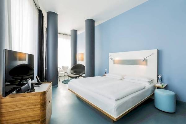 Ein modernes Hotelzimmer im Ku Damm 101 mit einem großen Bett, Fernseher und minimalistischem Design.
