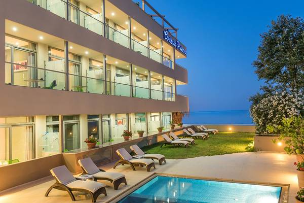 Außenansicht des Corissia Princess Hotels bei Abend, mit Swimmingpool und Sonnenliegen.