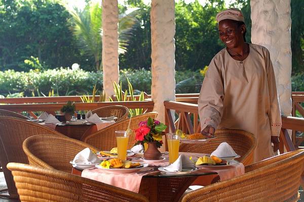 Frühstück auf der Terrasse im Pinewood Beach Resort & Spa mit einer lächelnden Bedienung.