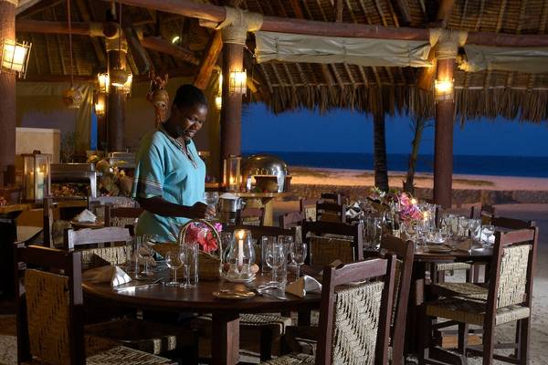 Ein Abendessen im Restaurant des Pinewood Beach Resort & Spa mit gedeckten Tischen und einer lächelnden Kellnerin.