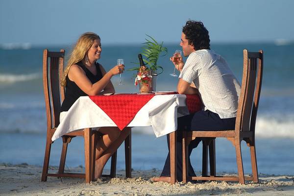 Ein Paar sitzt am Strand an einem Tisch mit einer Flasche und Gläsern.