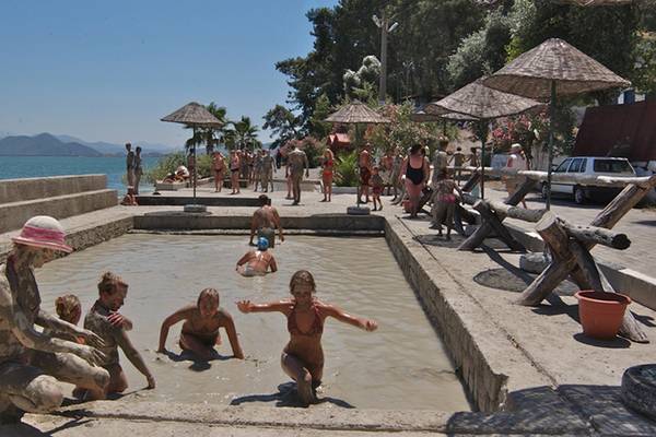 Gäste genießen das Schlammbad am Dalyan Resort Hotel, umgeben von Sonnenschirmen und lebhaftem Treiben.