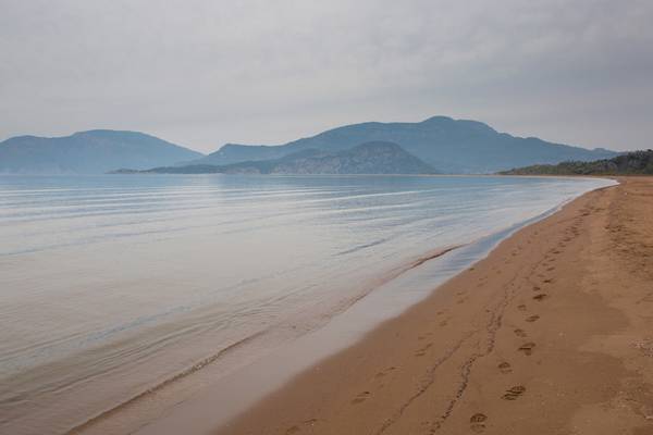 Strand mit blauem Wasser und Bergen im Hintergrund