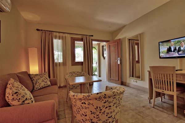Innenansicht eines Zimmers im Dalyan Resort Hotel mit Sofa, Fernseher und Schreibtisch.