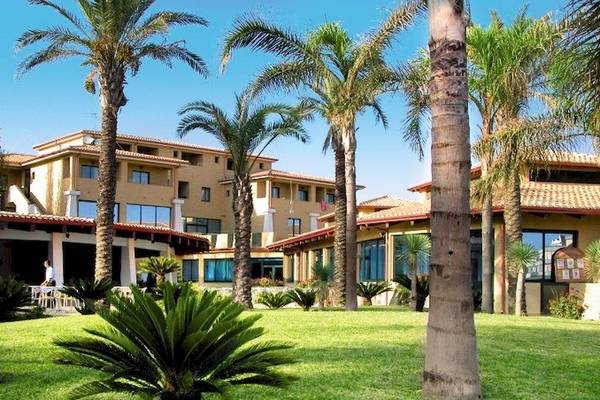 Außenansicht des TH Le Castella - Baia degli Dei Village Hotels mit Palmen und grüner Rasenfläche.