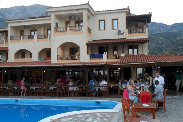 Gäste sitzen draußen an Tischen vor dem Kampos Village Resort Hotel mit Pool.