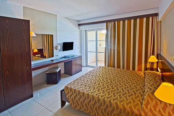Innenansicht eines Hotelzimmers im Akti Beach Club mit Bett, Schreibtisch und Fernseher.