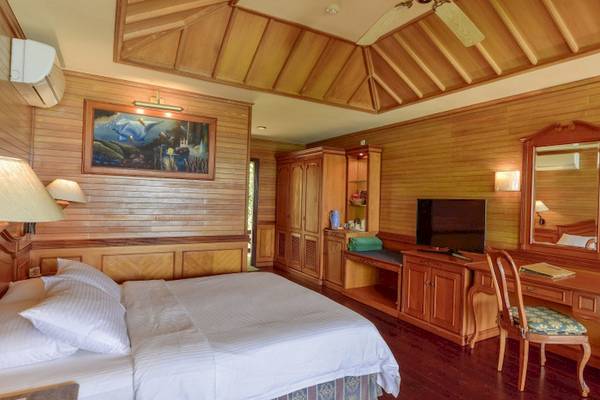 Innenansicht eines Hotelzimmers im Royal Island Resort & Spa mit Holzwänden, einem Bett, Fernseher, Schreibtisch und Möbeln.