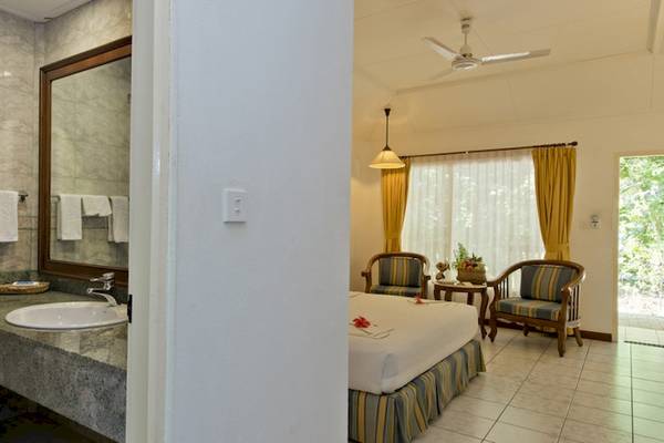 Ein Badezimmer im Royal Island Resort & Spa mit einem Waschbecken, Spiegel, Handtüchern, einem Bett, Stühlen und einer Terrasse.