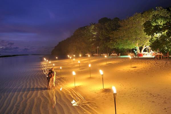 Paar auf einem sandigen Strand des Royal Island Resorts und Spa bei Nacht mit vielen brennenden Fackeln