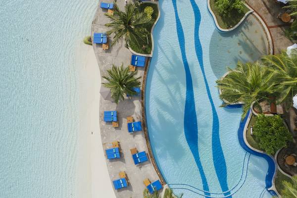 Luftaufnahme des Pools im Royal Island Resort & Spa mit weißen Liegen und blauem Wasser.
