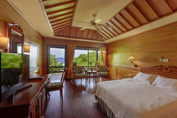 Schlafzimmer im Royal Island Resort & Spa mit Doppelbett, Fernseher, Holzmöbeln und Terrassenzugang.