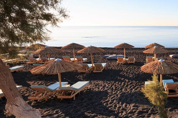 Strand mit vielen Sonnenliegen und Sonnenschirmen, Blick auf das Meer und eine Segelyacht in der Ferne.