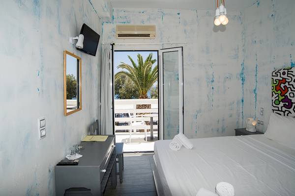 Ein modernes Hotelzimmer mit blau gestrichenen Wänden, einem Bett, einem Fernseher und einem Balkon mit Blick auf eine Palme.
