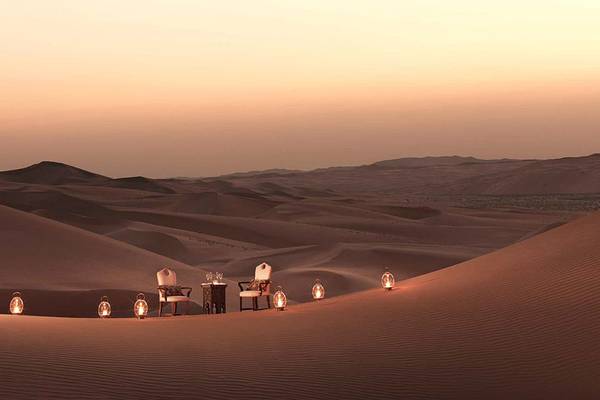 Sonnenuntergang im Qasr Al Sarab Desert Resort by Anantara mit zwei Stühlen und Tisch in der Wüste.