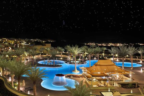 Nachtansicht des Qasr Al Sarab Desert Resort von Anantara mit beleuchteten Palmen und Swimmingpools.
