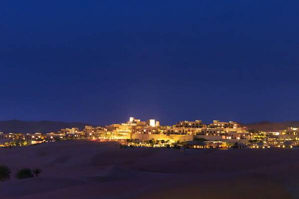 Nachtansicht des Qasr Al Sarab Desert Resort by Anantara, das in der Wüste von Al Sharqiyah leuchtet.