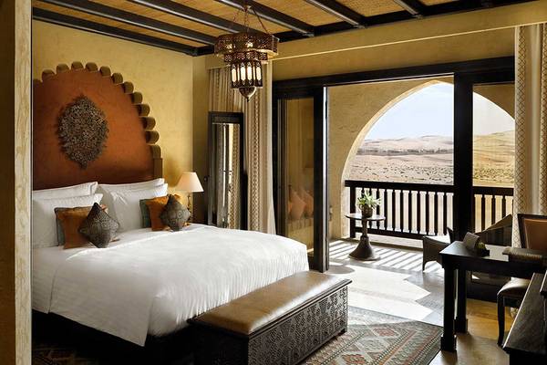 Innenansicht eines Hotelzimmers im Qasr Al Sarab Desert Resort by Anantara mit einem großen Bett und Blick auf die Wüste.