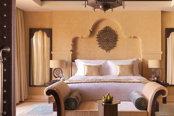 Hotelzimmer im Qasr Al Sarab Desert Resort by Anantara mit einem großen Bett, goldenen Dekor und zwei Beistelltischen mit Lampen.