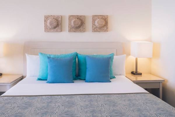 Doppelbettzimmer im Iberostar Selection Cancun Hotel mit zwei Nachttischen, Lampen und drei dekorativen Wandpaneelen.