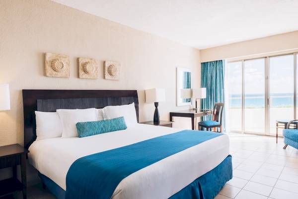 Ein modernes Hotelzimmer im Iberostar Selection Cancun mit Blick auf das Meer und einem großen Bett.