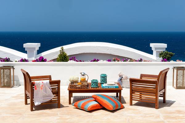 Terrasse mit Meerblick im Mitsis Grand Hotel Beach, mit zwei Holzstühlen, einem Tisch und Kissen.