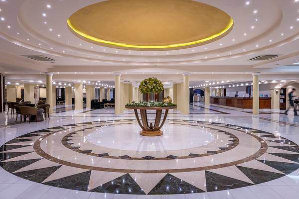 Die geräumige Lobby des Mitsis Grand Hotel Beach mit einer zentralen Blumeninstallation und gemustertem Boden.