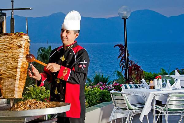 Mann schneidet Fleisch auf einer Terrasse mit Blick auf das Meer.