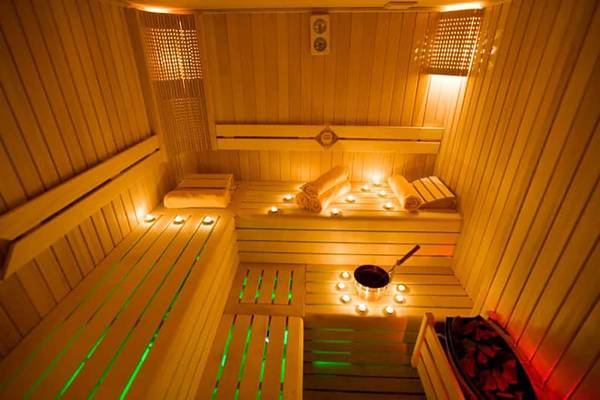 Sauna im Fantasia Hotel De Luxe mit Holzbänken, Kerzen und grünen Lichtern.
