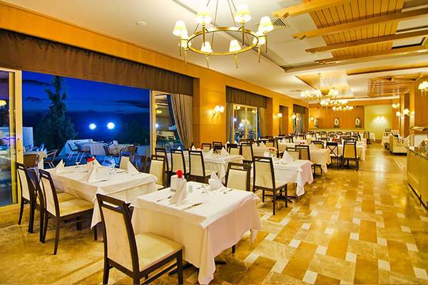 Innenansicht des Restaurants im Fantasia Hotel De Luxe mit gedeckten Tischen und abendlicher Außenbeleuchtung.