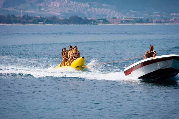 Familie genießt Bananaboot-Fahrt auf dem Meer mit einem Boot im Hintergrund