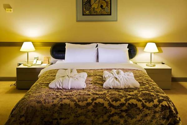 Fantasia Hotel De Luxe - Bett mit zwei weißen Bademänteln, aufgezogen auf einem bedruckten Bettlaken.