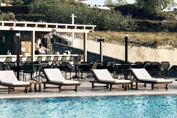 Pool-Loungebereich des Santo Pure Oia Suites & Villas Hotels mit Sonnenliegen und einer Bar.