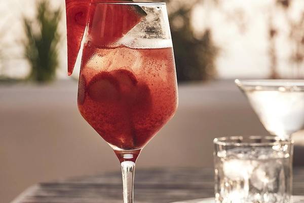 Ein Glas mit einem roten Cocktail und einem Stück Wassermelone auf einem Tisch mit weiteren Gläsern.