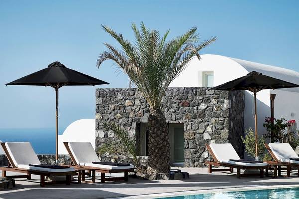 Pool-Lounge-Bereich des Santo Pure Oia Suites & Villas mit Sonnenliegen, Palme und Sonnenschirmen.