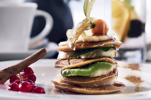 Frühstück im Santo Pure Oia Suites & Villas mit Pfannkuchen, Früchten und Zimtstange auf einem weißen Teller.