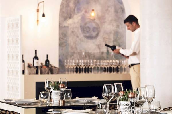 Ein Mann in einem weißen Hemd serviert Wein in einem Restaurant des Santo Pure Oia Suites & Villas Hotels.