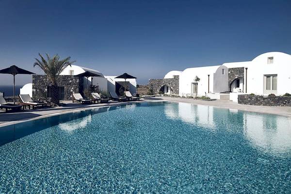 Außenpoolbereich des Santo Pure Oia Suites & Villas Hotels mit weißen Gebäuden und Sonnenliegen.