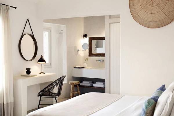 Santo Pure Oia Suites & Villas Schlafzimmer mit weißem Bett, Tisch, Stuhl und Badezimmerspiegel.