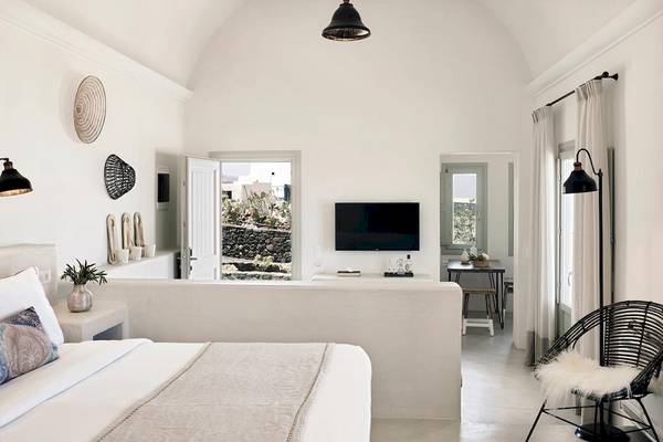 Innenansicht eines Schlafzimmers im Santo Pure Oia Suites & Villas Hotel mit weißen Wänden, einem großen Bett und einer Fernsehwand.
