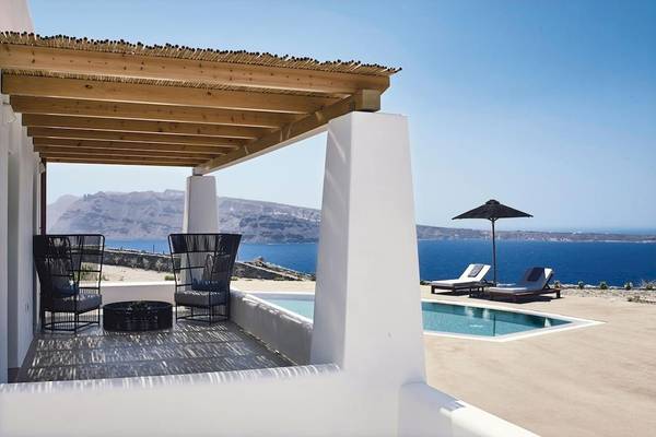 Terrasse des Santo Pure Oia Suites & Villas mit Blick auf das Meer, zwei Stühle, Tisch und Sonnenschirm.