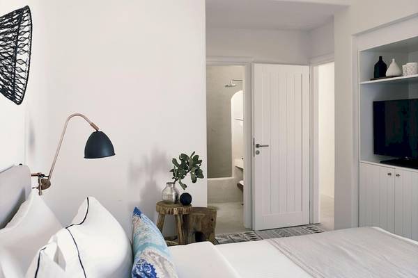 Schlafzimmer im Santo Pure Oia Suites & Villas mit weißem Bett, Kissen, Tisch und Lampe