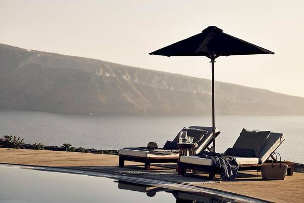 Außenbereich des Santo Pure Oia Suites mit Liegestühlen und einem Schirm am Pool.
